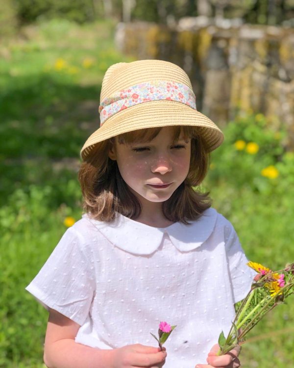 petite fille portant un chapeau de paille orné d'un lien en liberty et une blouse blanche à col claudine en plumetis.
