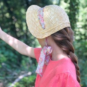 Jeune fille portant un chapeau de paille rétro avec un lien en Liberty et une robe rose en double gaze de coton.