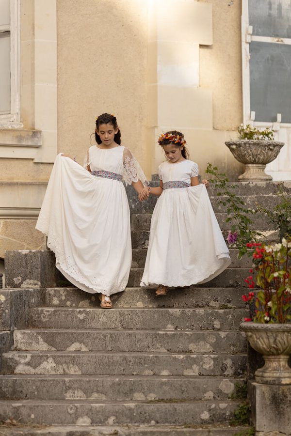 petites filles portant des robes longues et blanches de cérémonie. Elles descendent les escaliers d'un chateau