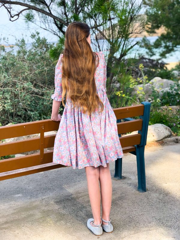 Jeune fille portant une robe à col et manches volantés en Liberty Meadow Song pétales.