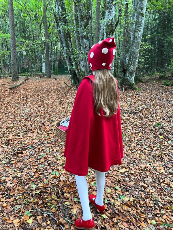 Le petit chaperon rouge se promenant dans la forêt vêtue d'une cape et d'un bonnet rouge.