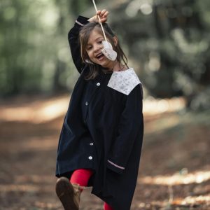 petite fille se promenant dans la forêt. elle est vêtue d'une robe en velours milleraies bleu marine à col carré et de collants rouges